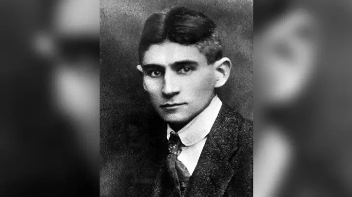 A black and white portrait of a young man with short, dark hair, wearing a tweed jacket and tie.