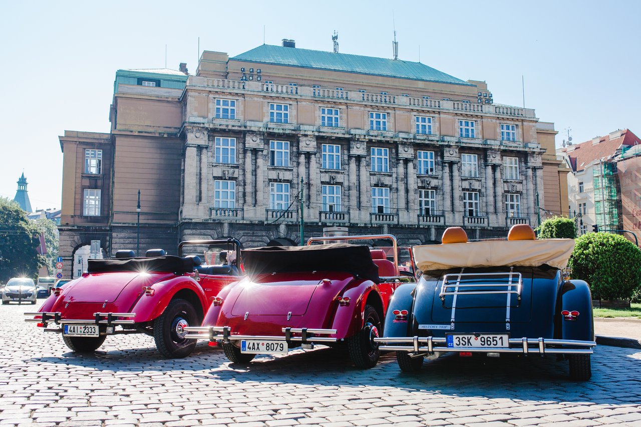Three vintage cars parked with their backs to the camera, in front of the magnificent university