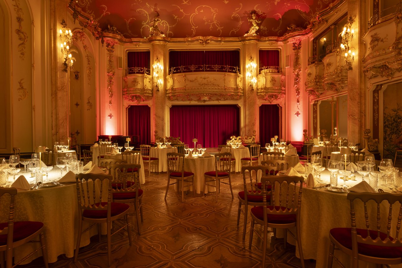 A two-story dining room adorned with statues and gold, bathed in soft, subdued light, with a stage at the back