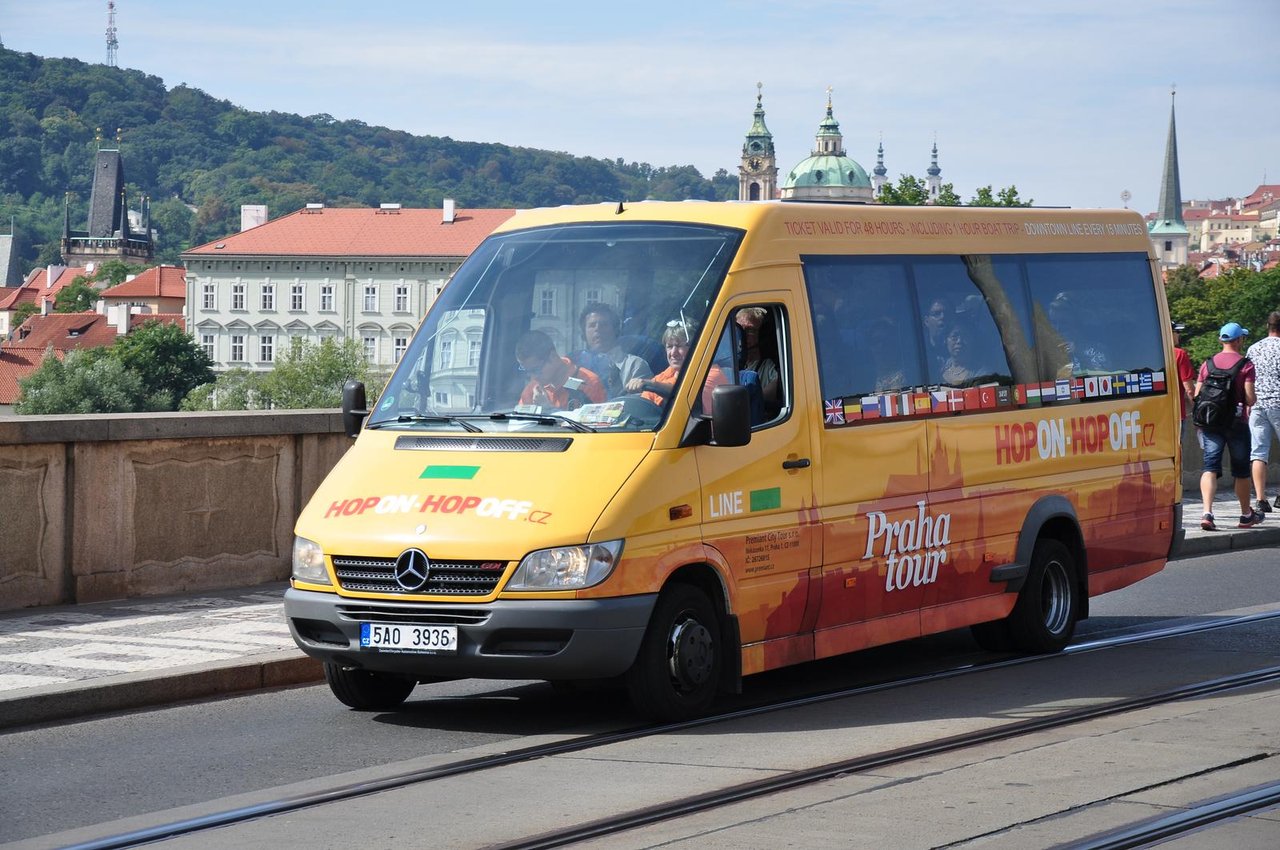 An orange tourist minibus passes by, carrying tourists on board.
