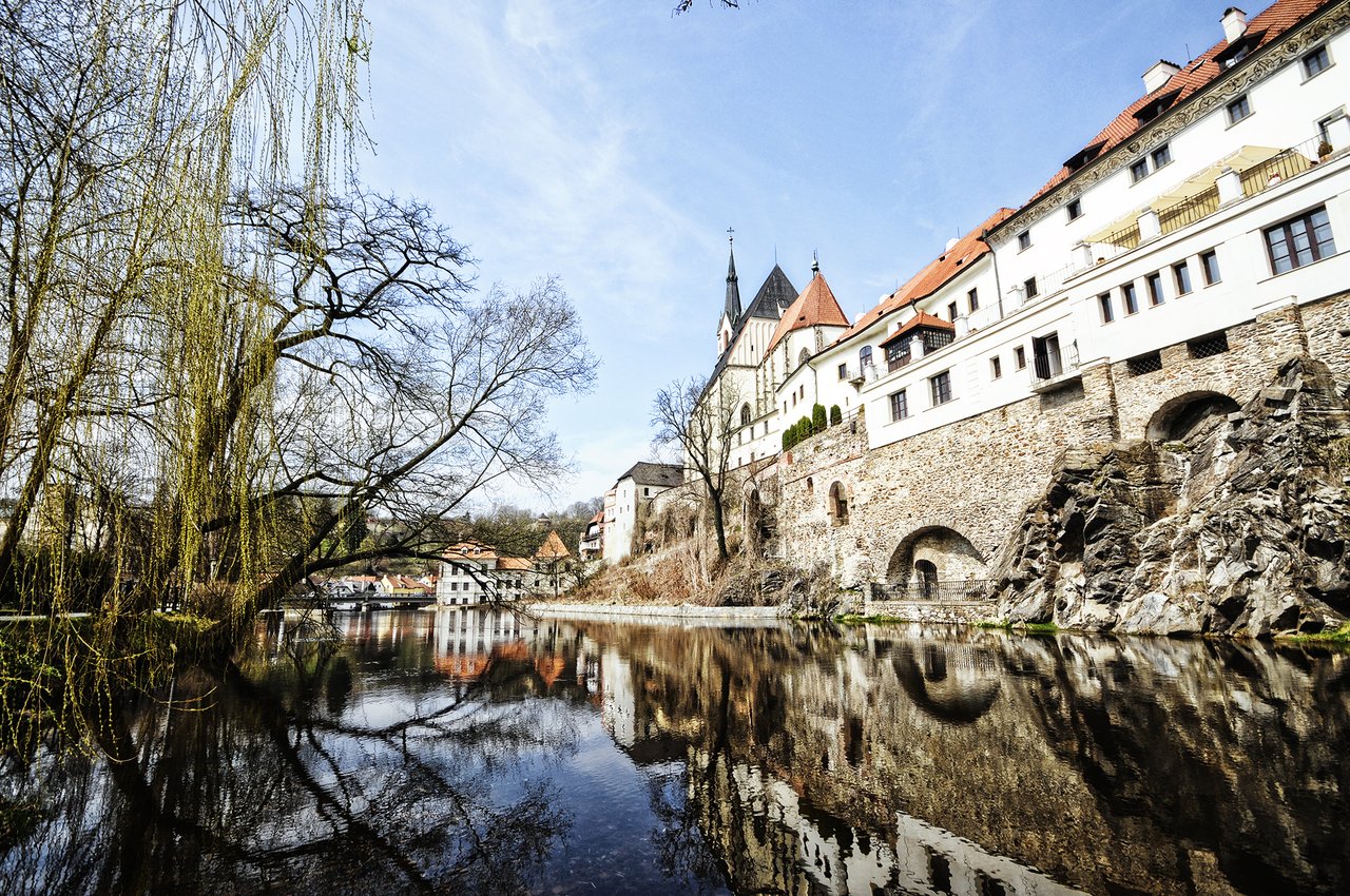 A medieval stone fortress with white walls and a red roof, overlooking a river