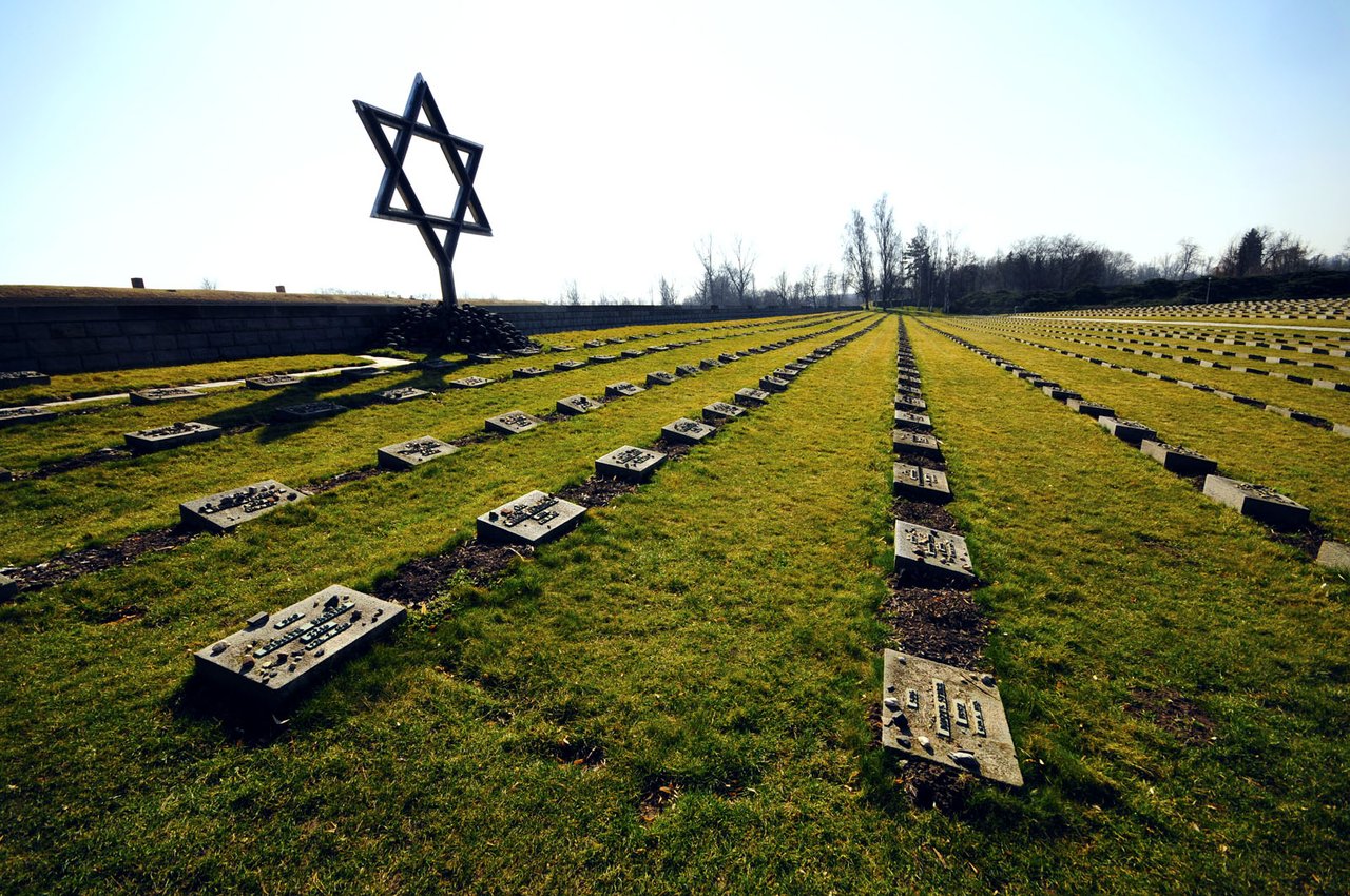 Hundreds of gravestones in the cemetery, overlooked by a large metal Star of David under a clear sky.