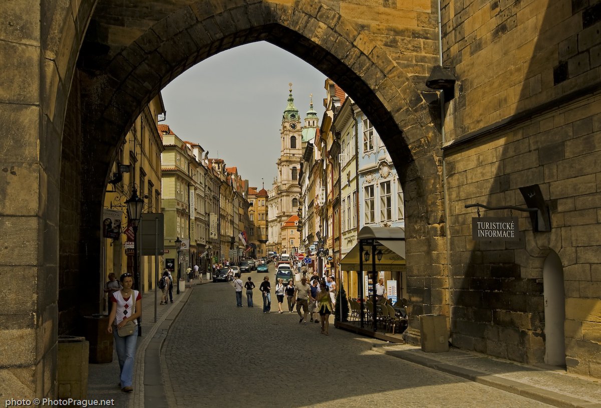 A monumental stone arch,a cobblestone street lined with colorful facades that winds its way up toward the bell tower of a large church